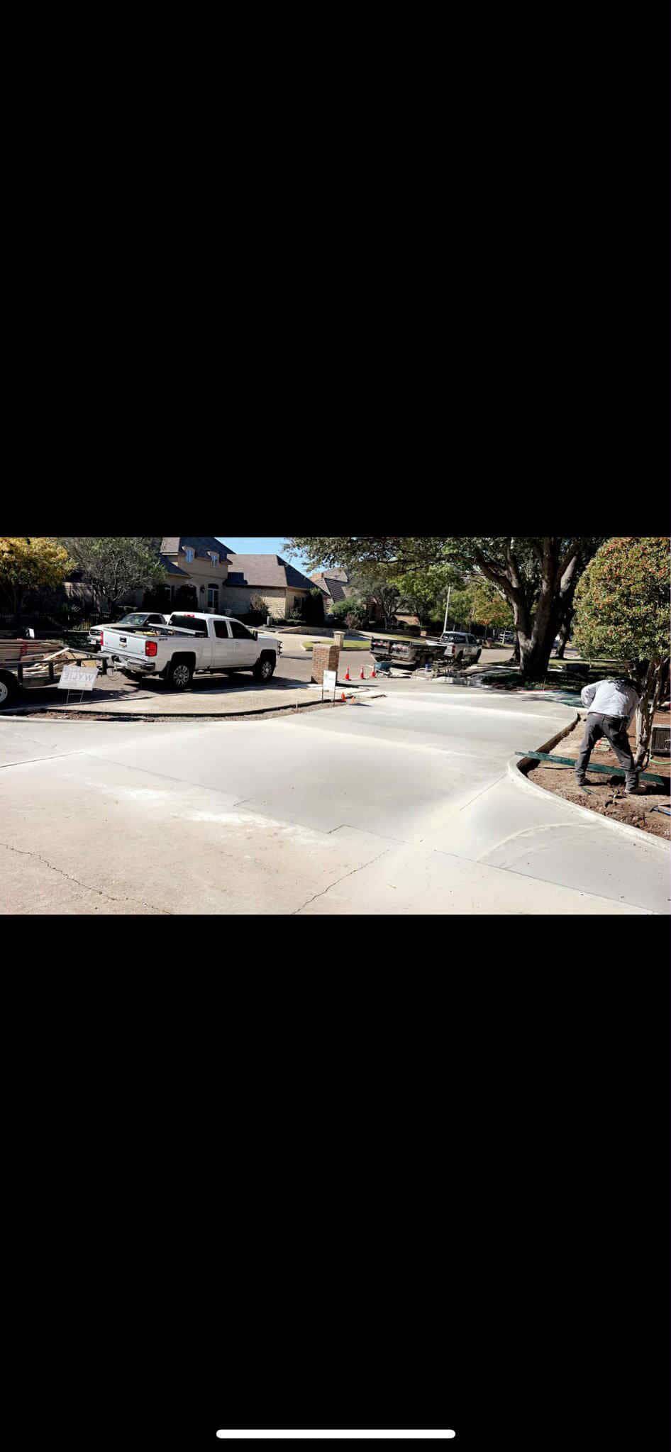 Person blowing debris off a paved surface near a white truck, houses, and trees.
