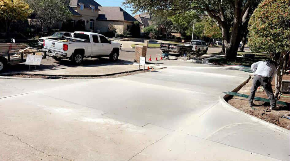 Concrete driveway being poured by a construction worker, surrounded by trucks, in a residential neighborhood.