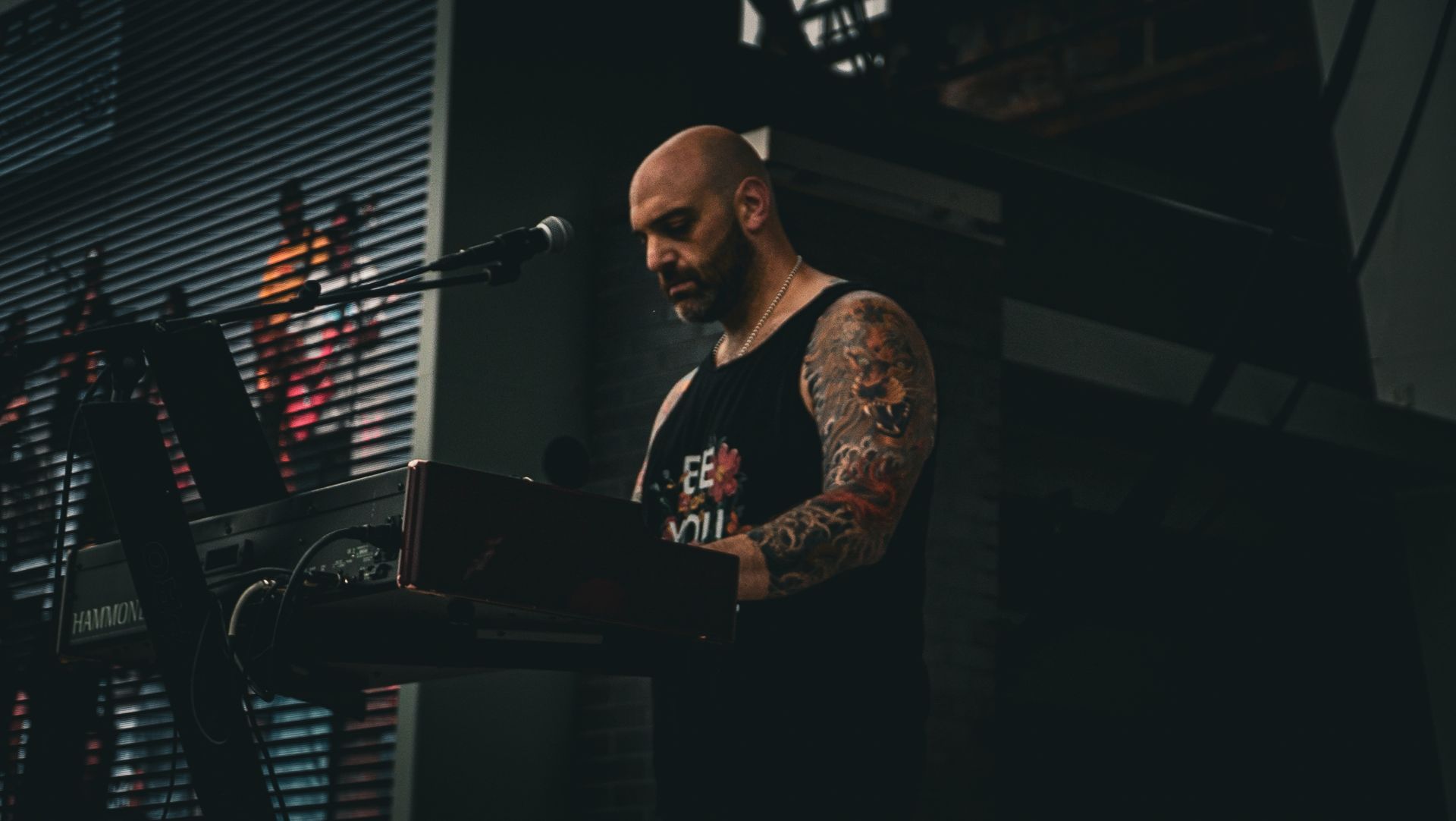 A bald man with tattoos is playing a keyboard and singing into a microphone.