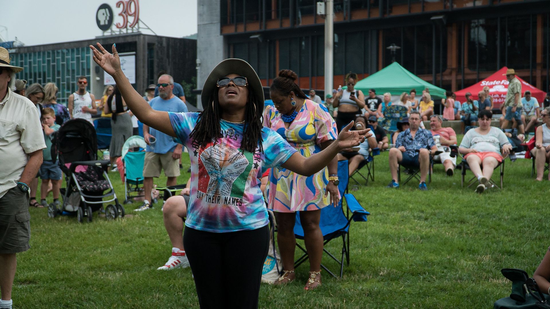 A woman is standing in a field with her arms outstretched in front of a crowd of people.