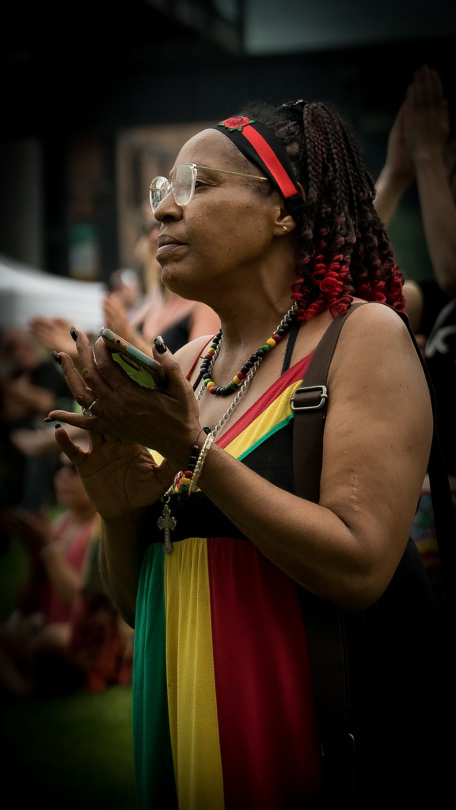 A woman in a colorful dress is holding her hands together in a crowd.