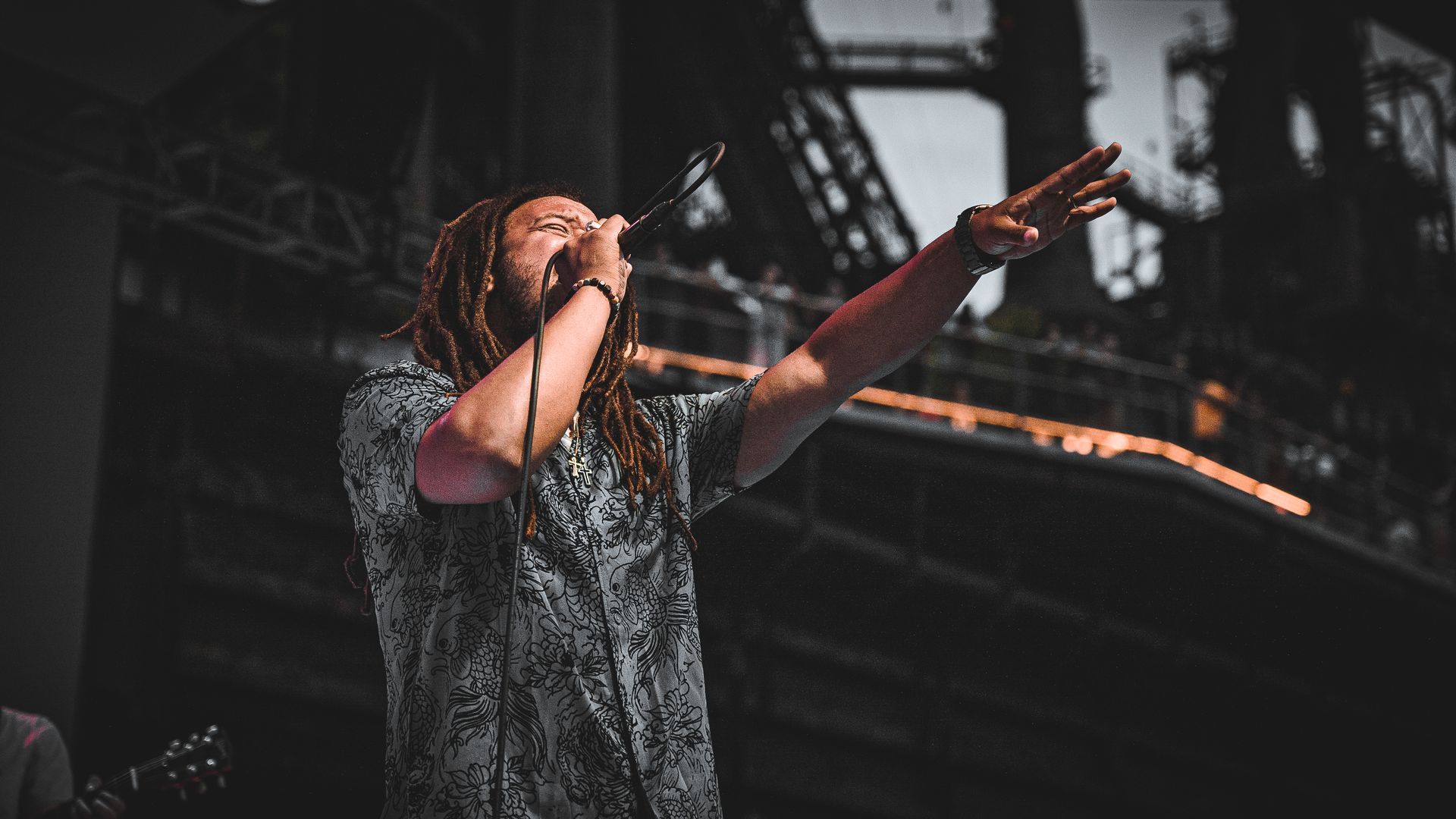 A man with dreadlocks is singing into a microphone on a stage.