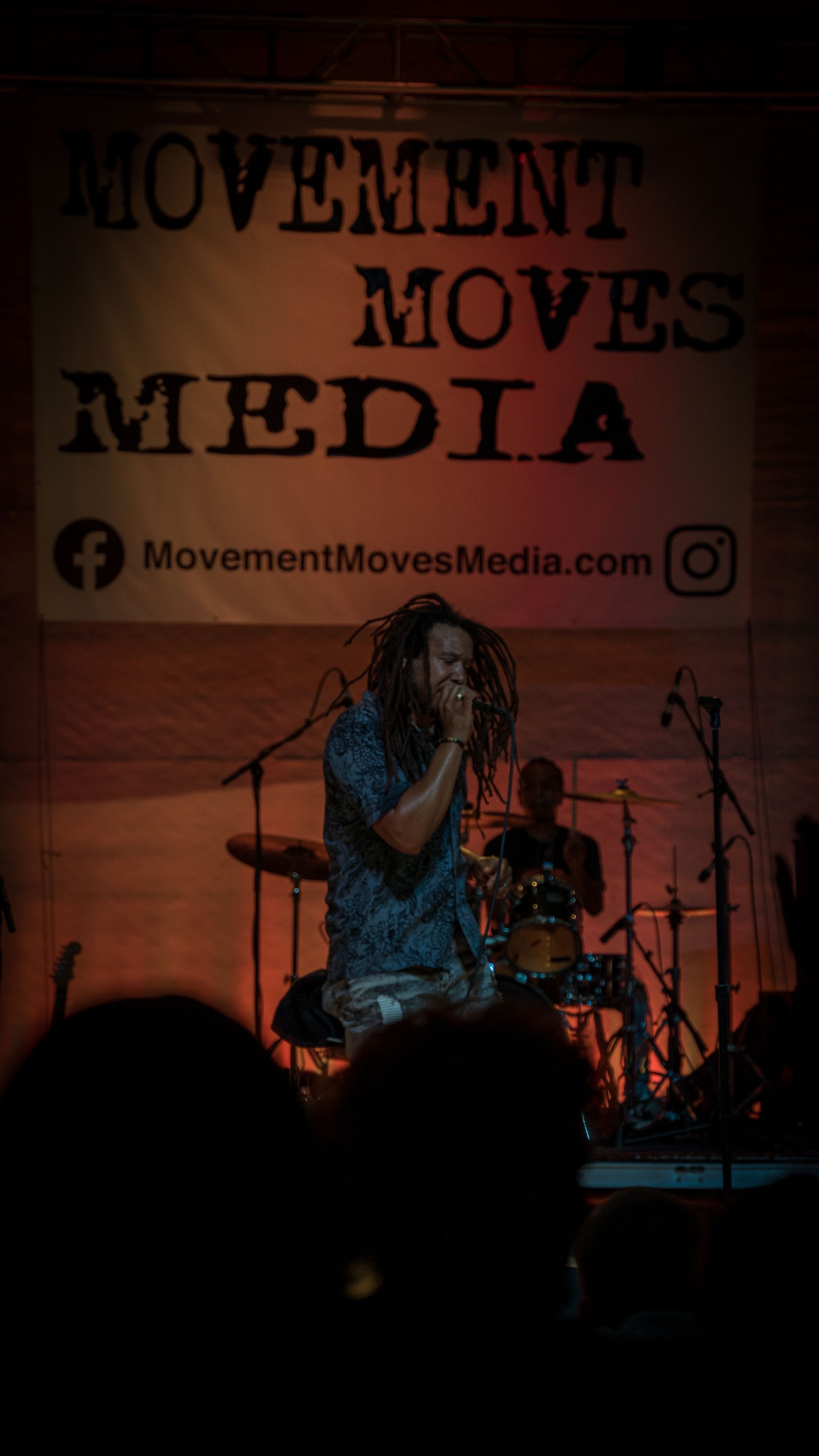 A man is singing into a microphone in front of a sign that says movement moves media.