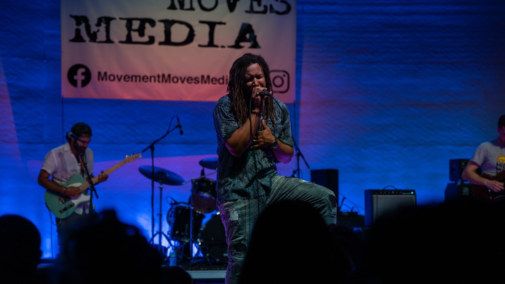 A man with dreadlocks is singing into a microphone on a stage in front of a crowd.