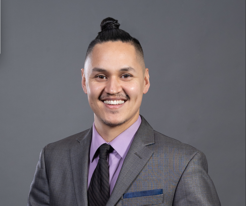 A man in a black shirt and a bun is standing in a field.