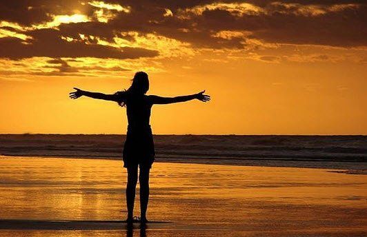 一个身影伫立在沙滩上，张开双臂，映衬着金色的夕阳洒在海面上。
