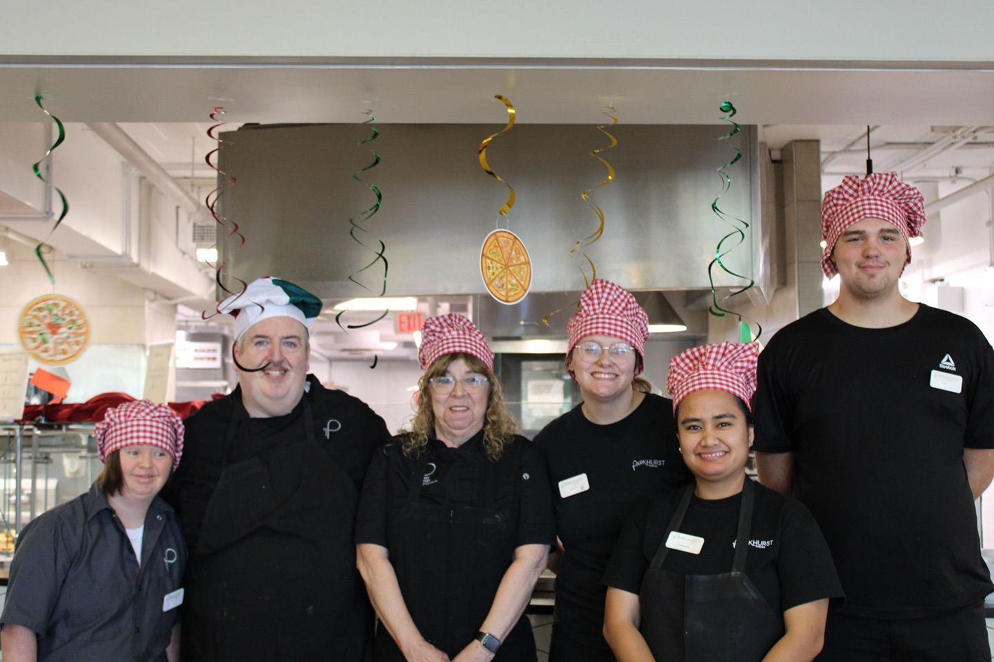 Group of seven people in kitchen attire posing, some wearing chef hats.