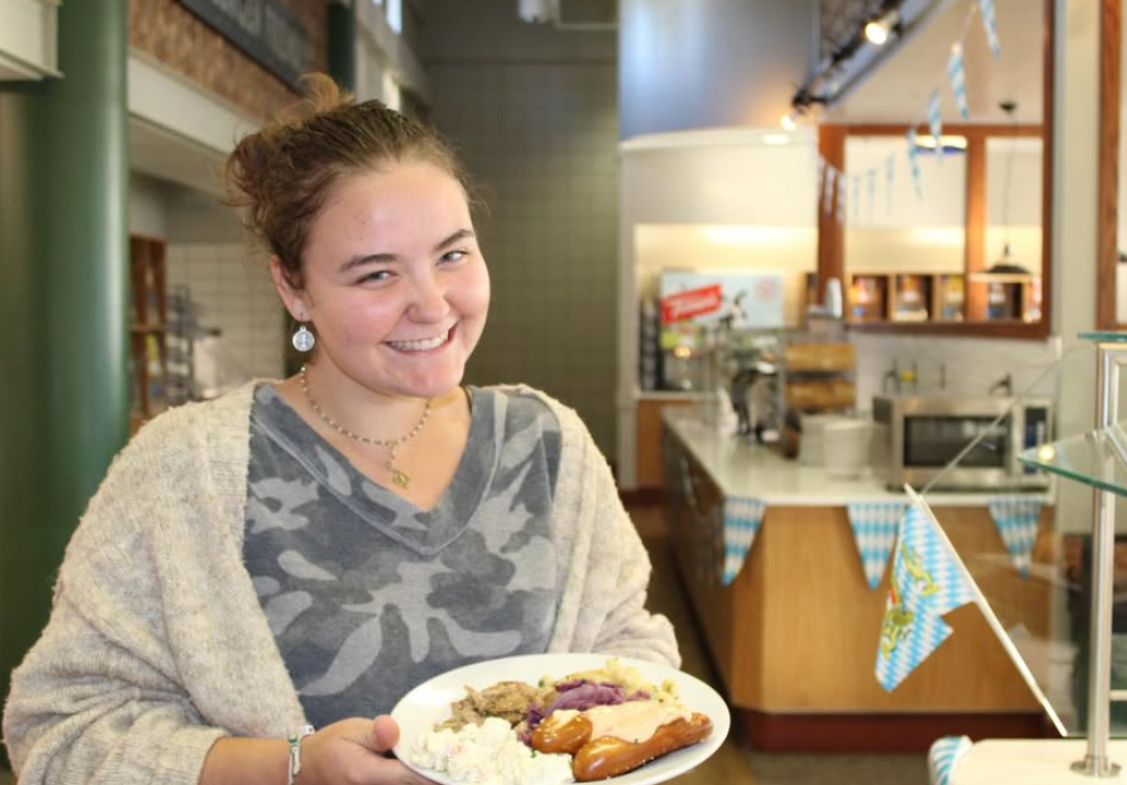 A grl holding a plate of german food including sausages. 