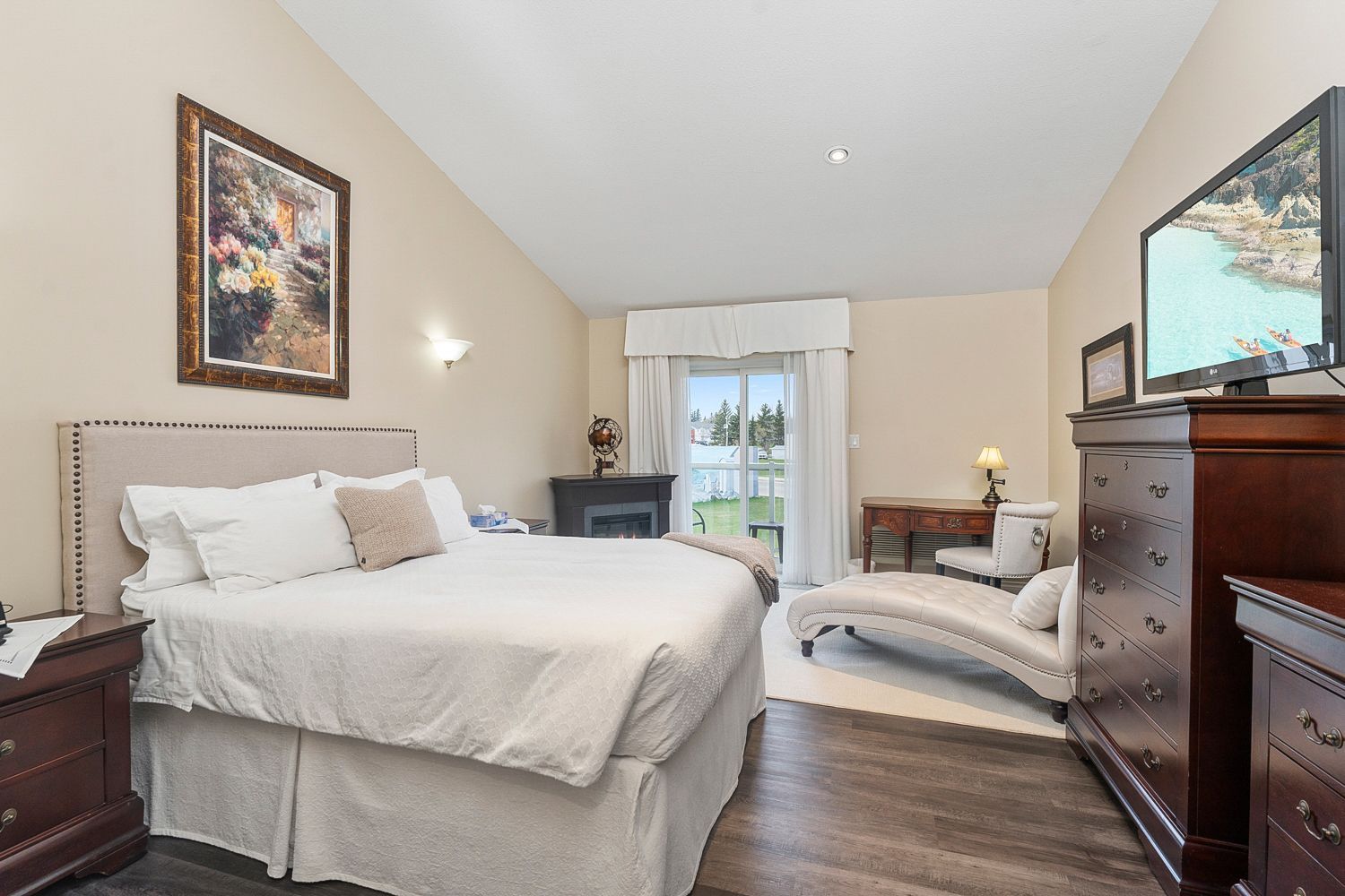 A bedroom with a queen sized bed, flat screen tv, balcony, and lake view