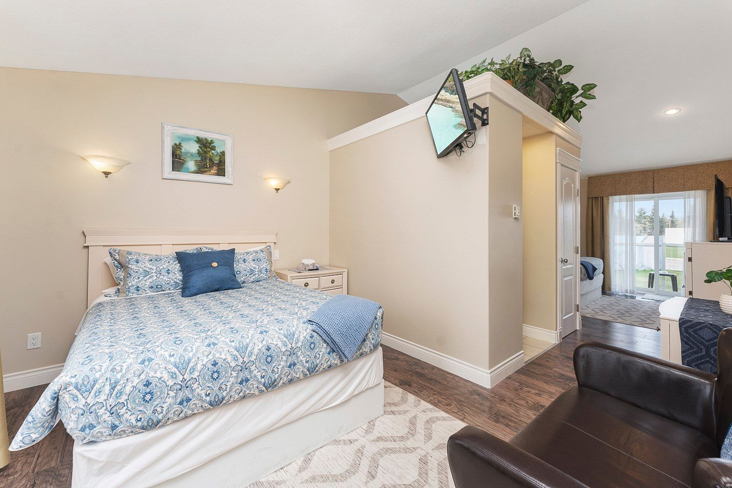 A bedroom with a queen bed, balcony with lake view, and a television on the wall.