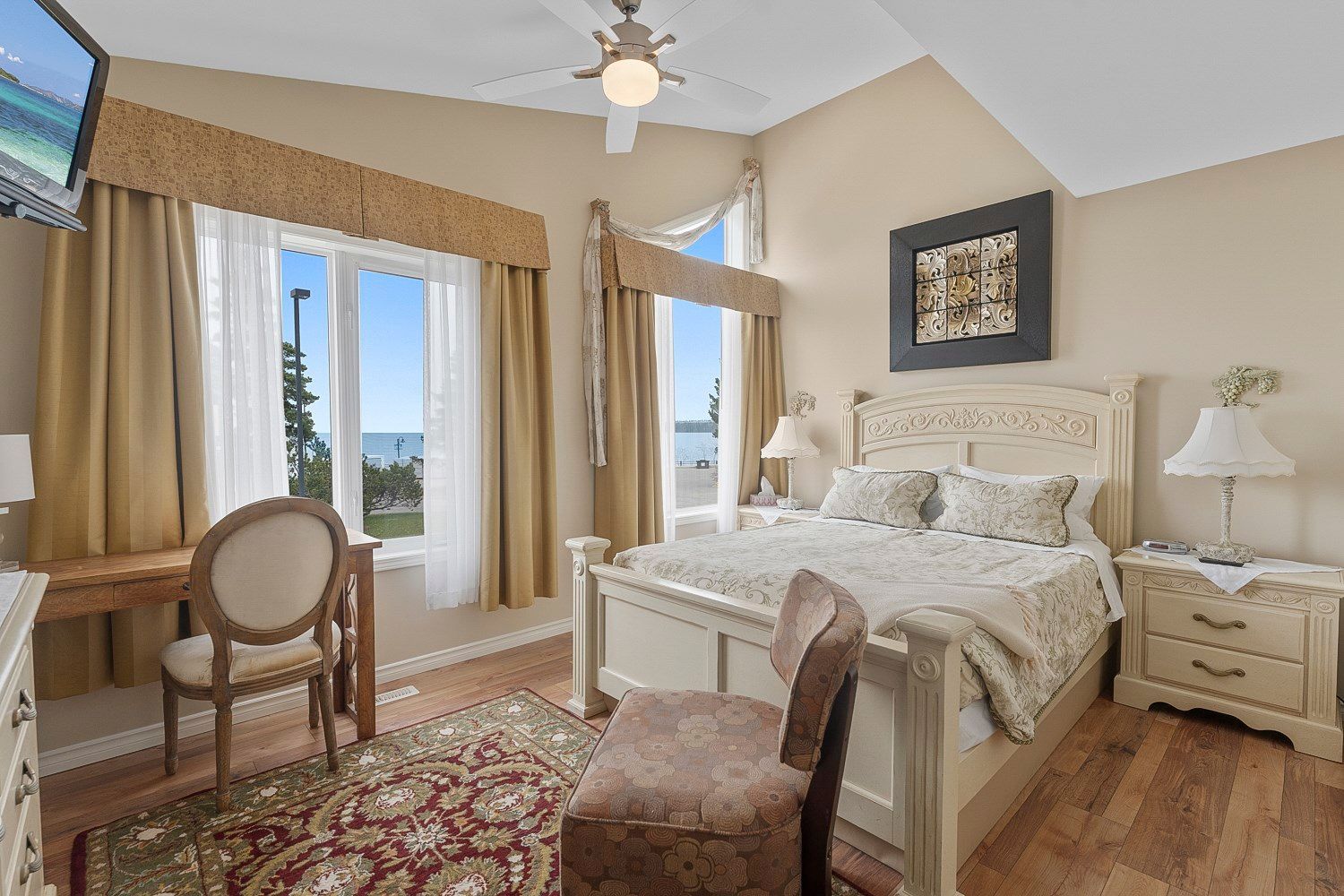 A bedroom with a queen bed, chair , desk, television, and view of the lake. Lakeshore Inn Bed & Breakfast