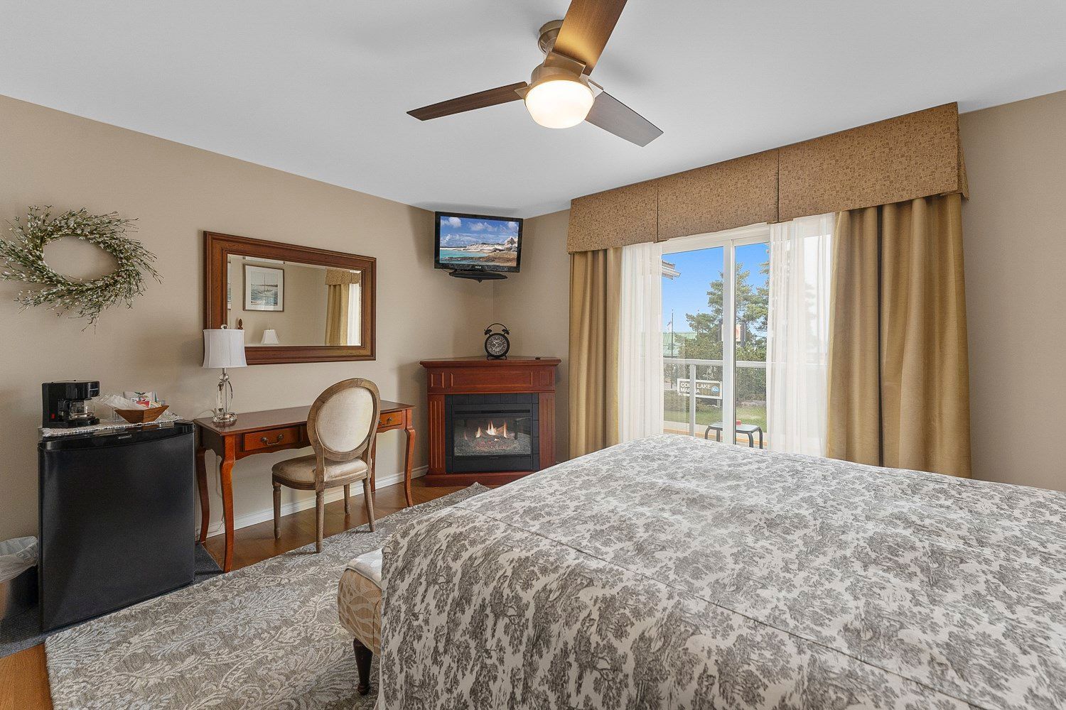 A bedroom with a queen size bed , fireplace , desk, television, and view of the lake from the balcony. 