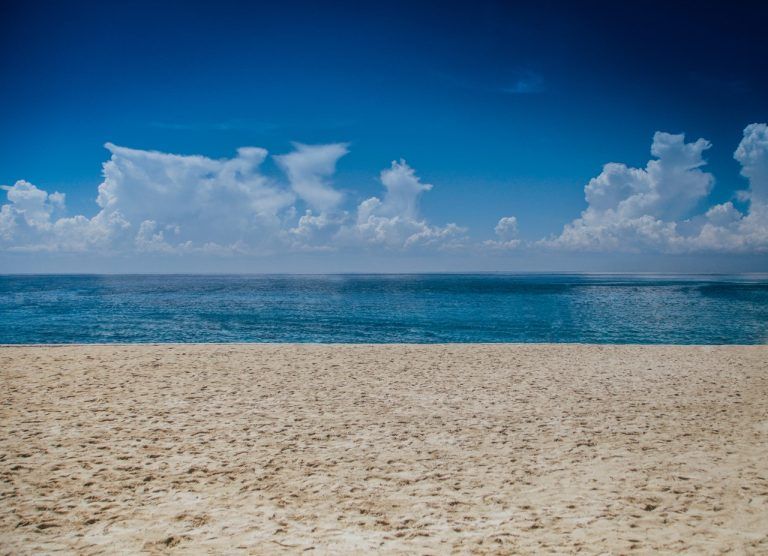 An empty beach with a blue sky and clouds overlooking the ocean.