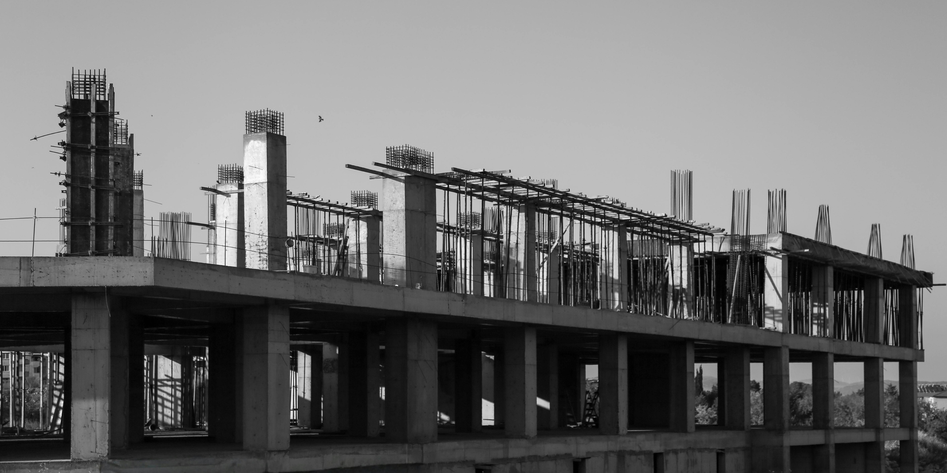 A black-and-white view of a concrete building frame under construction with vertical rebar extending from the roof.