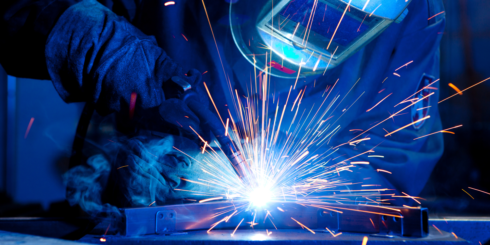An angle grinder cuts through metal, creating a brilliant, high-contrast spray of bright orange sparks against a black background.