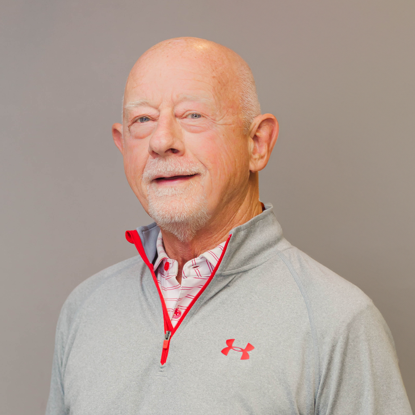 A man wearing a gray under armour sweater is standing with his hands in his pockets.