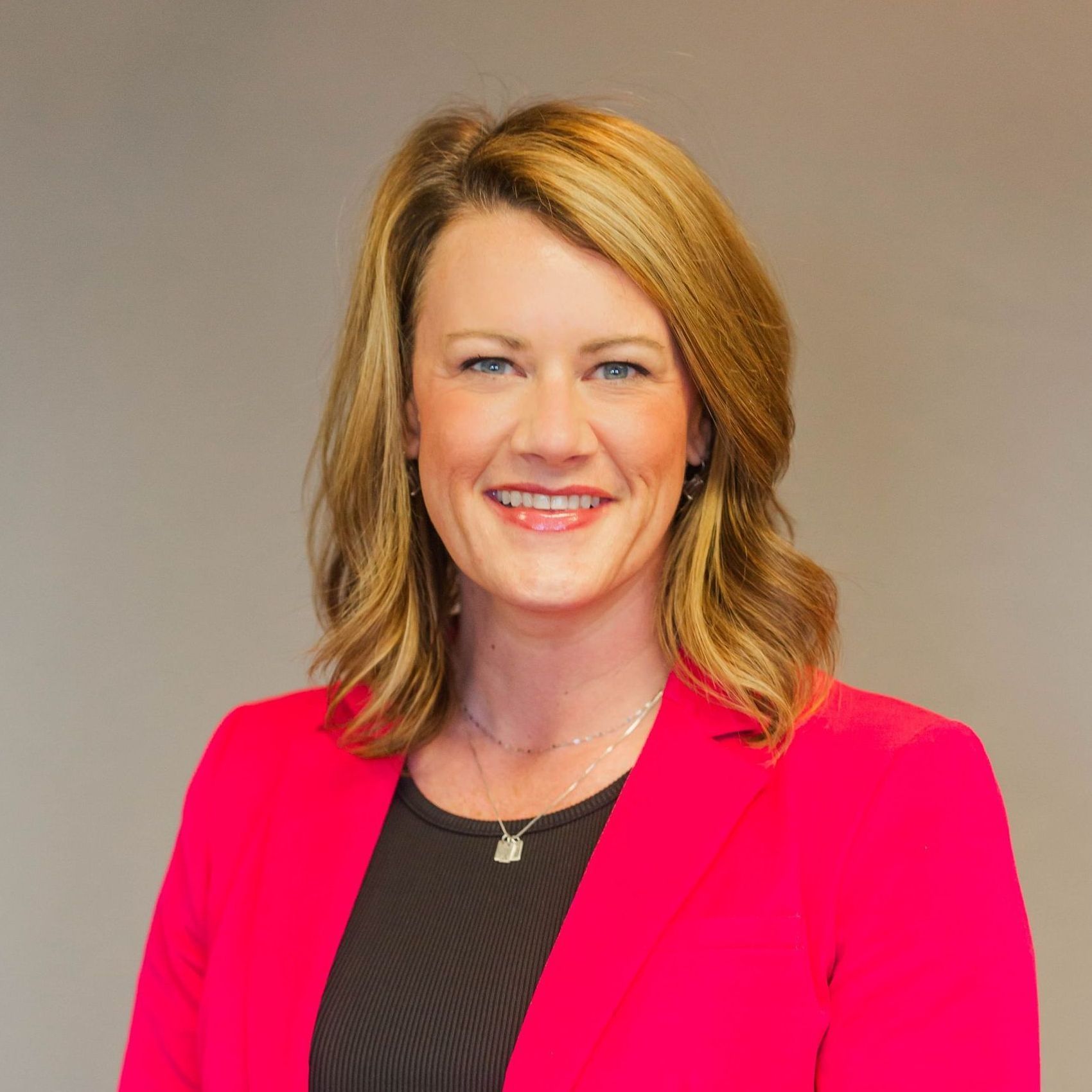 A woman is wearing a pink jacket and smiling for the camera.