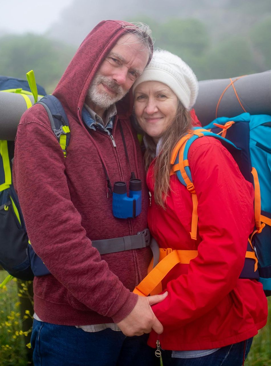 A man and a woman are holding hands while standing next to each other with backpacks.