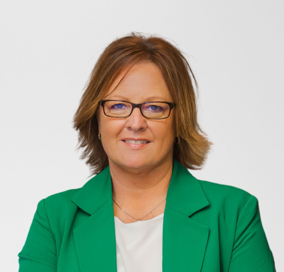 A woman wearing glasses and a green jacket is smiling