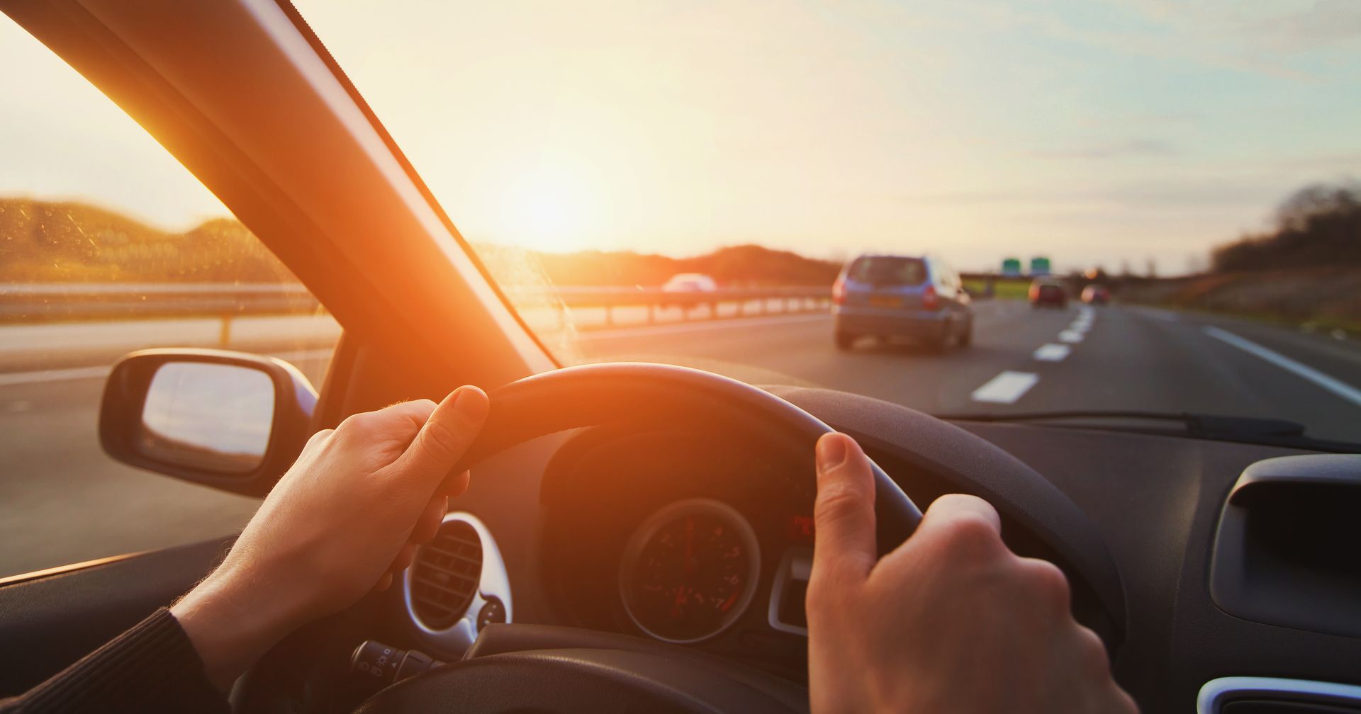Driver’s view from a car on a highway at sunset, hands on the steering wheel, vehicles ahead | Quality Auto Repair Tire & Auto Sales