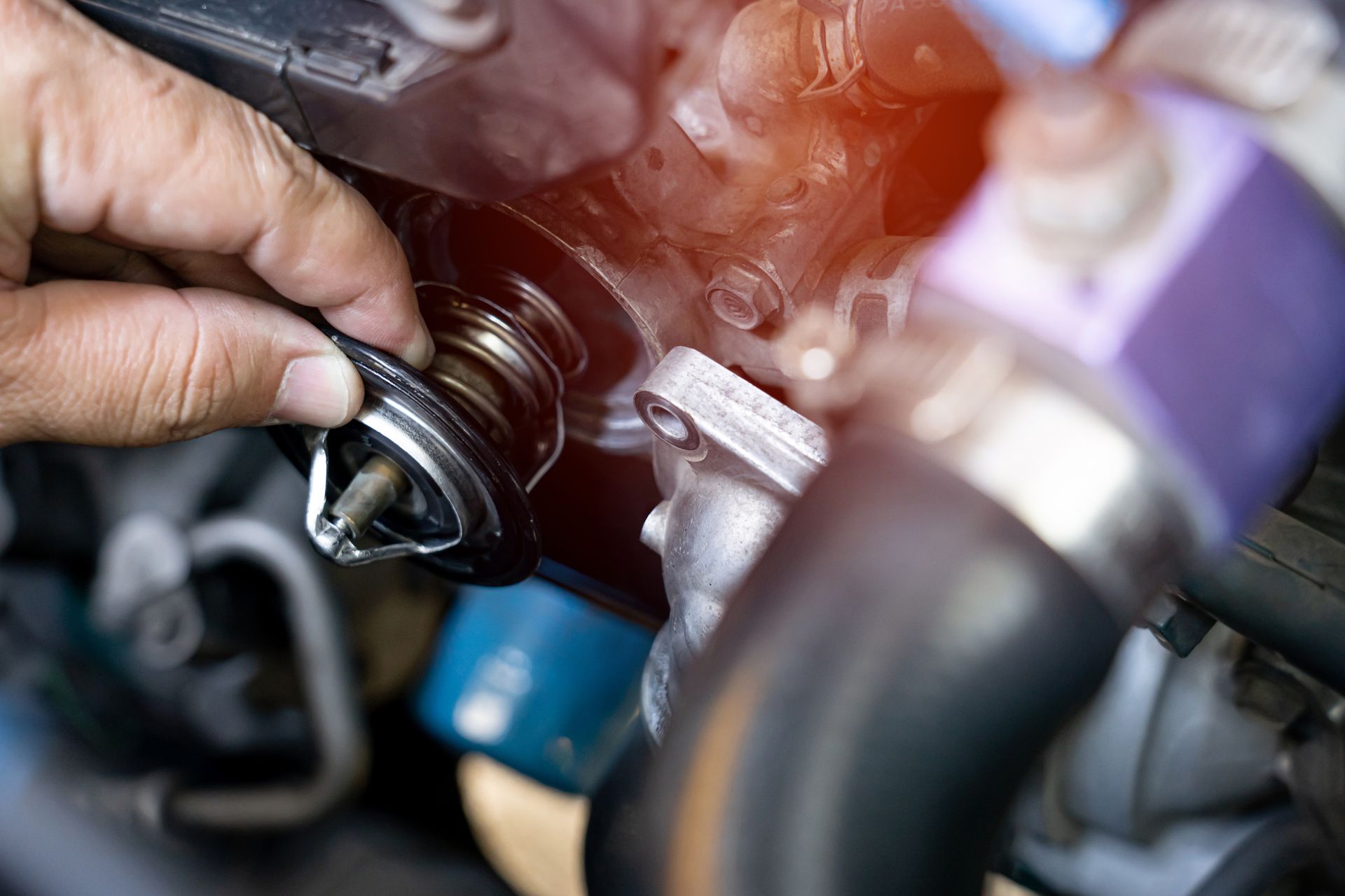 Hand tightening a metal cap on a car engine with visible hoses and components | Quality Auto Repair Tire & Auto Sales