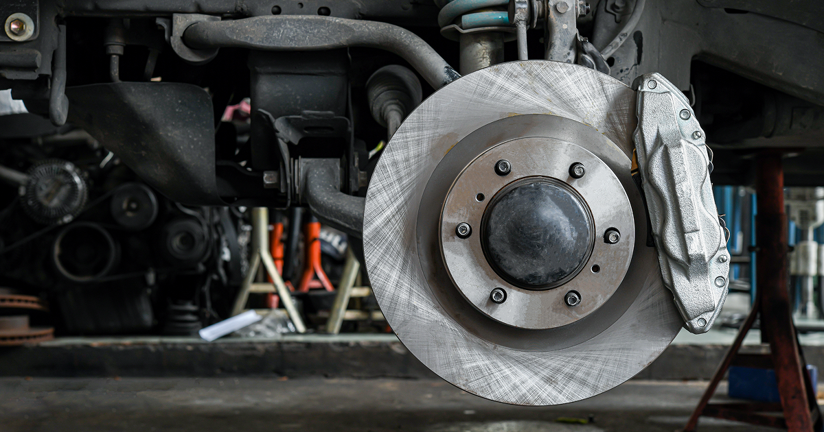 Car wheel and brake rotor assembly with silver protective wrap in a garage, seen from underneath the vehicle | Quality Auto Repair Tire & Auto Sales