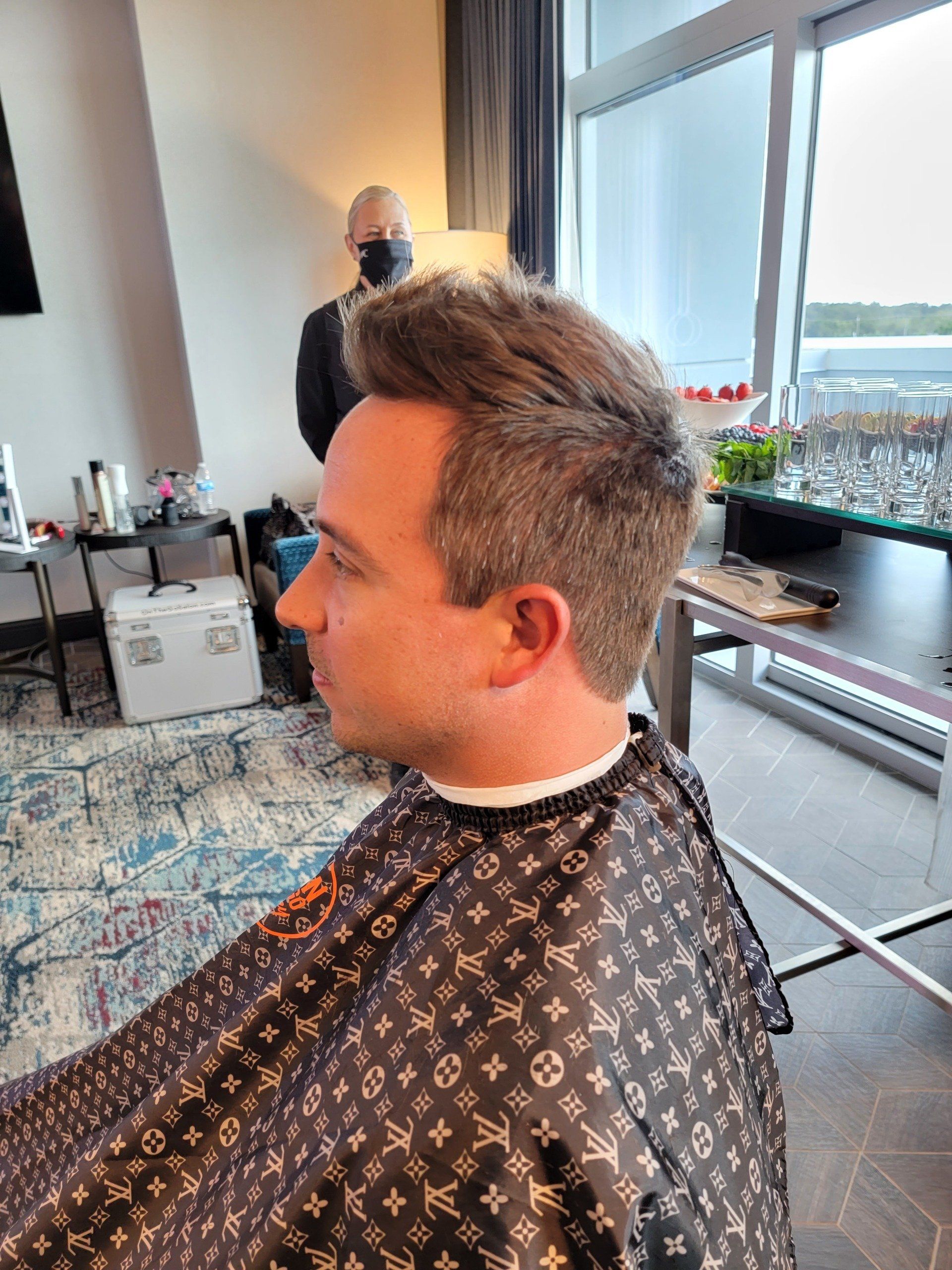 A man is getting his hair cut in a room with a louis vuitton cape.