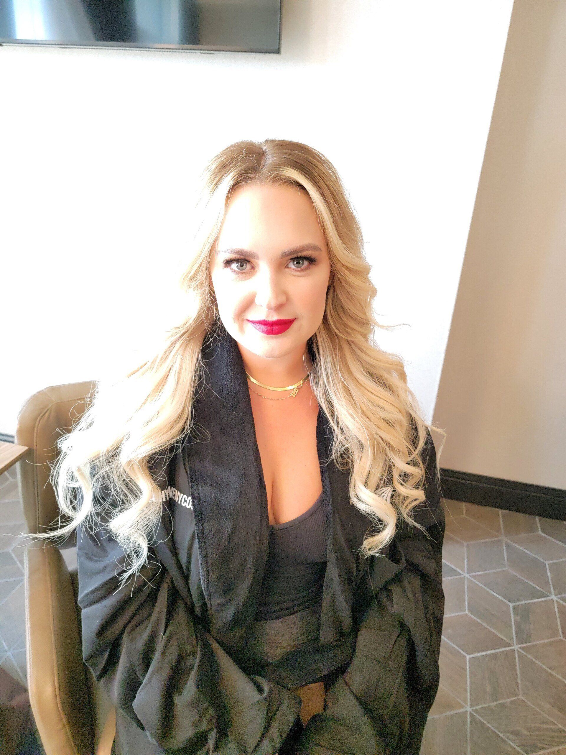 A woman with blonde hair and red lipstick is sitting in a chair.