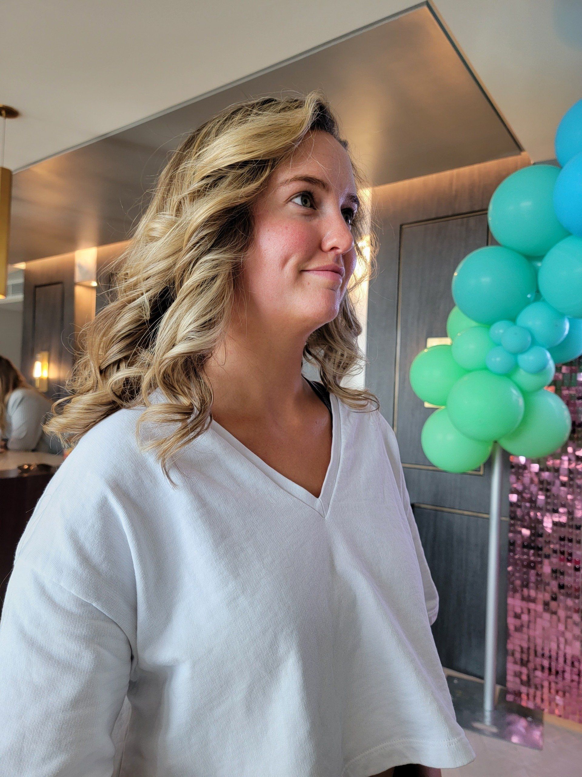 A woman in a white shirt is standing in front of a bunch of balloons.
