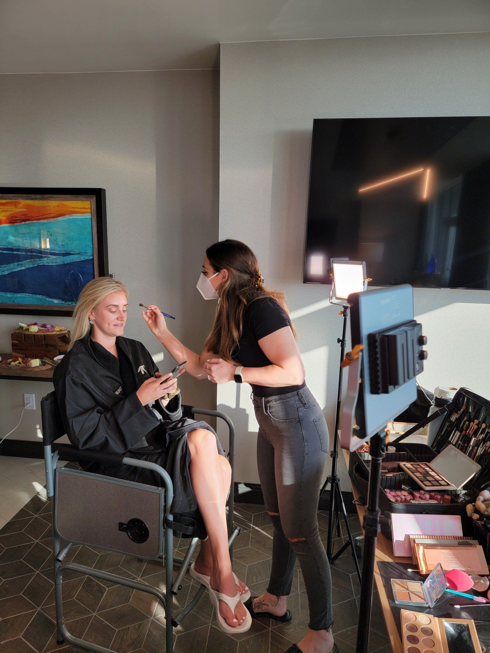 A woman is sitting in a chair getting her makeup done by a makeup artist.