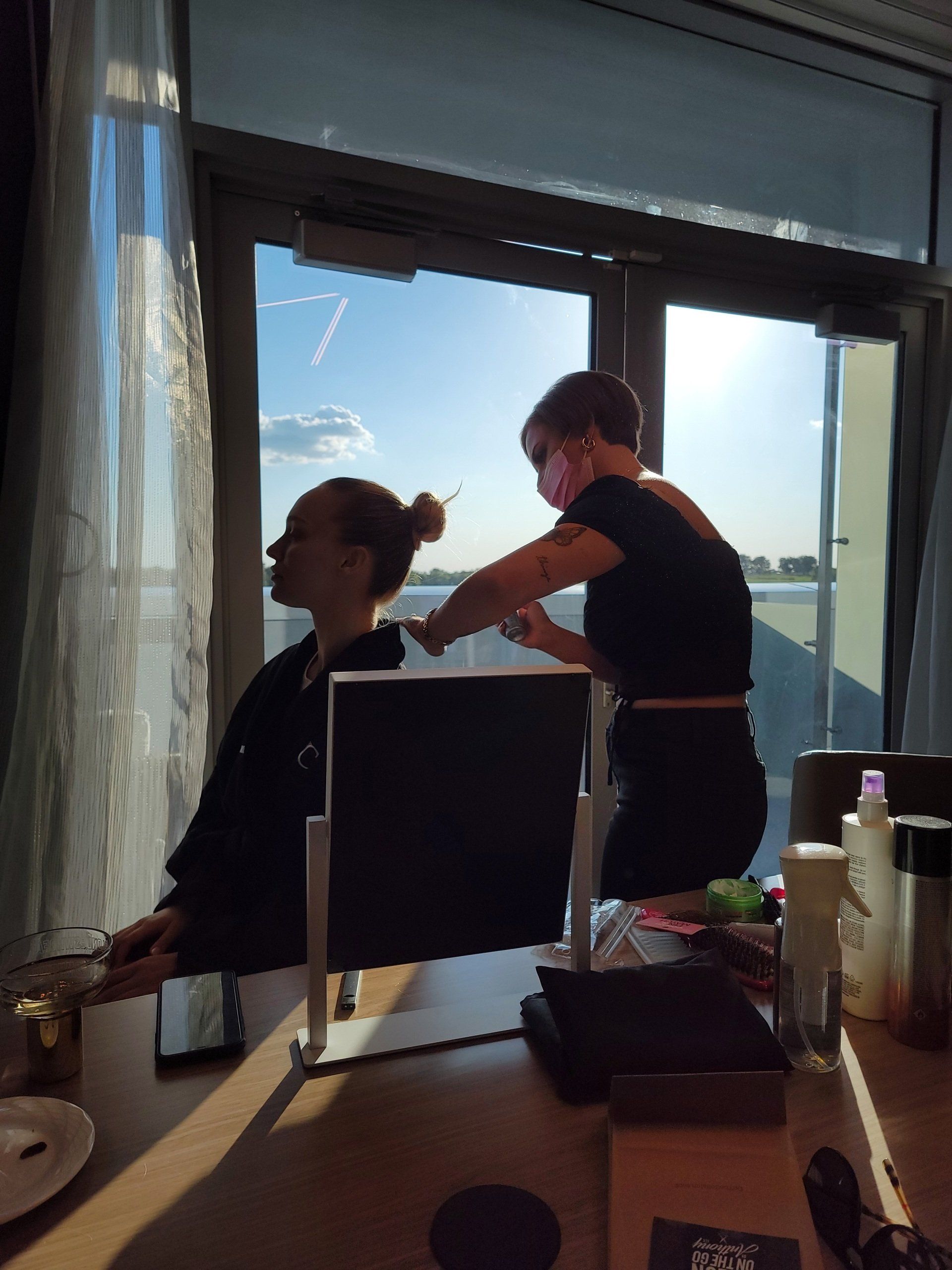 A woman is getting her hair done in front of a window