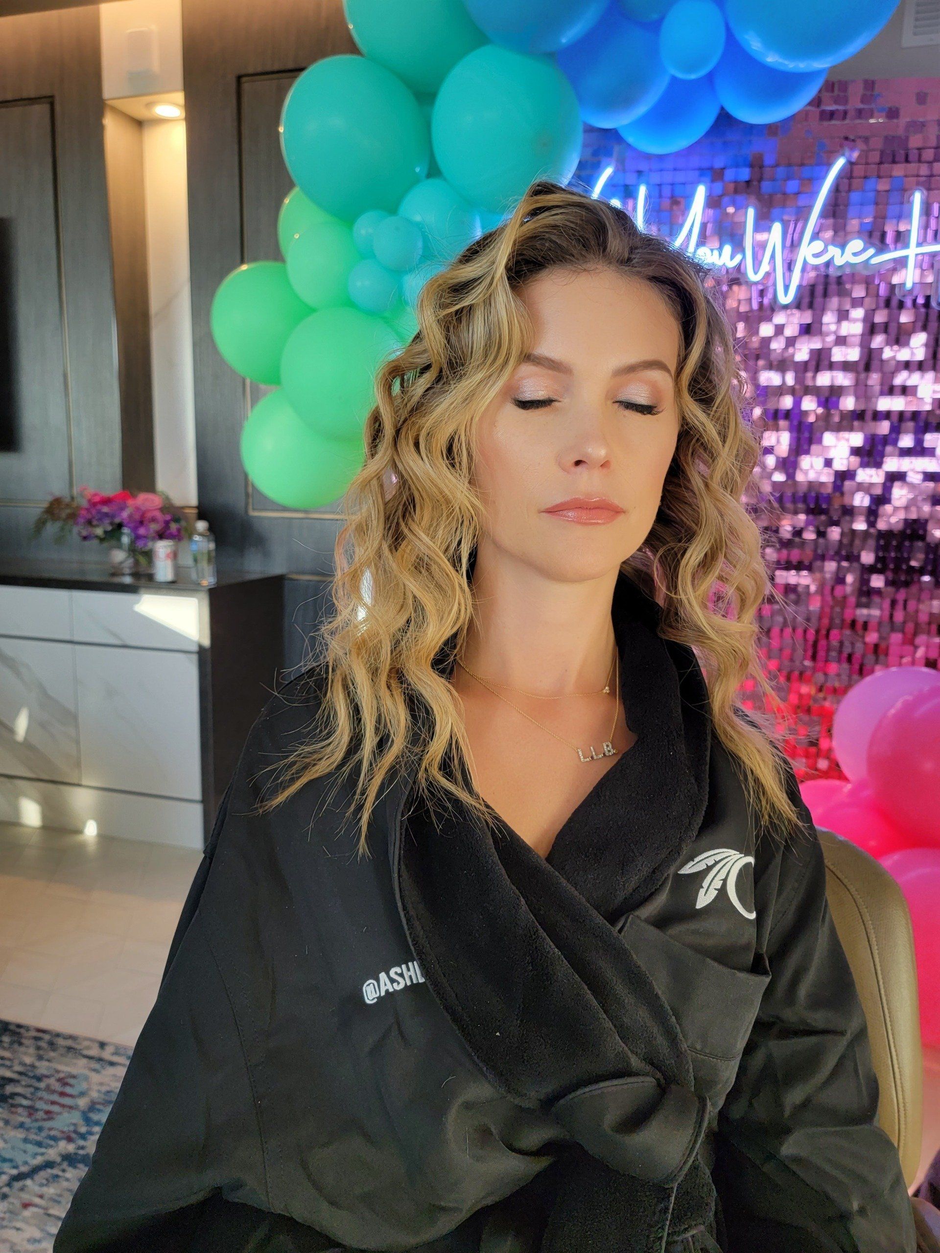 A woman in a black robe is sitting in front of a bunch of balloons.