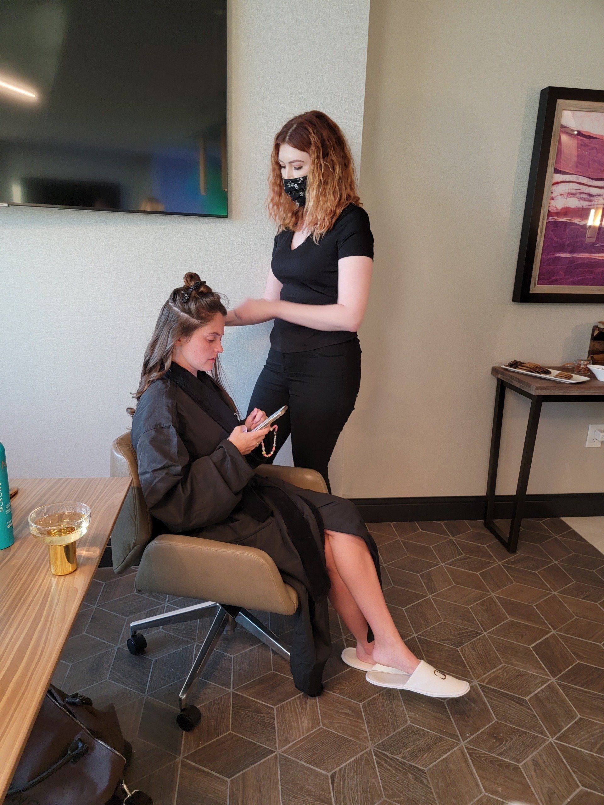A woman is getting her hair done in a salon while looking at her phone.