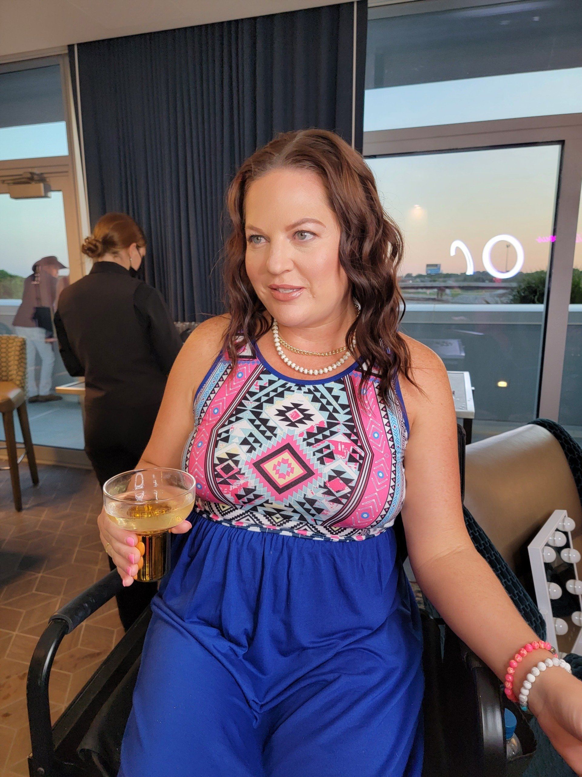 A woman in a blue dress is sitting in a chair holding a glass of wine.
