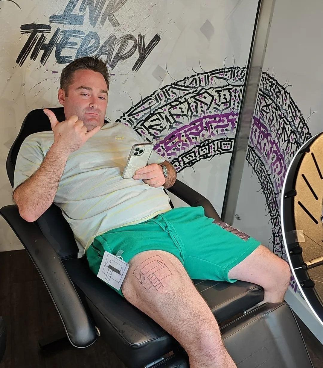 A man is sitting in a chair in front of a sign that says ink therapy