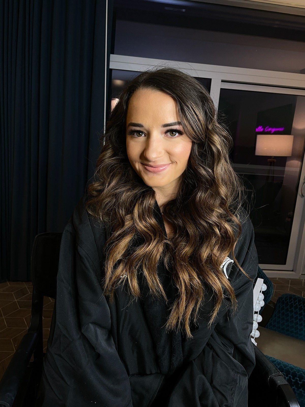 A woman in a black robe is sitting in front of a window.