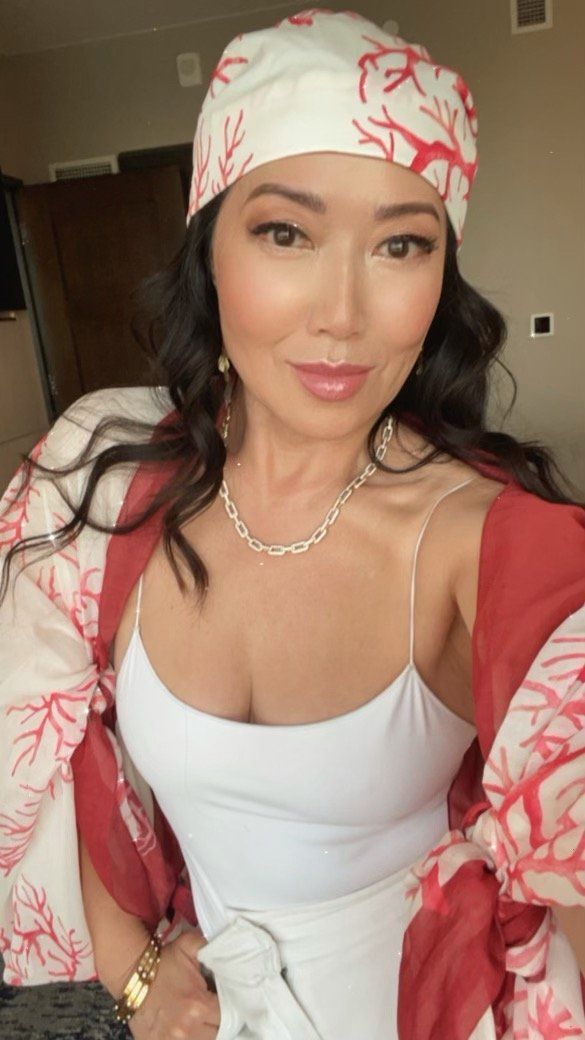 A woman wearing a white tank top and a red jacket is taking a selfie.