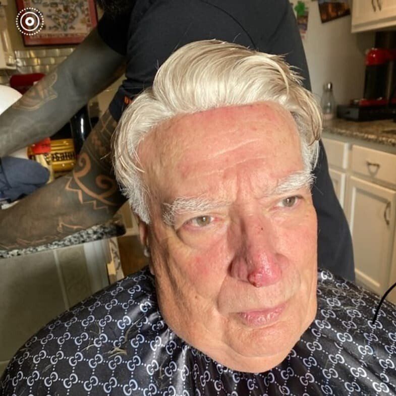 An older man is getting his hair cut in a kitchen