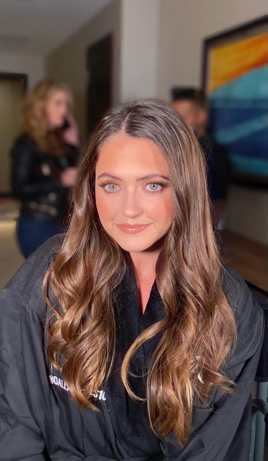 A woman with long brown hair and blue eyes is wearing a black jacket.