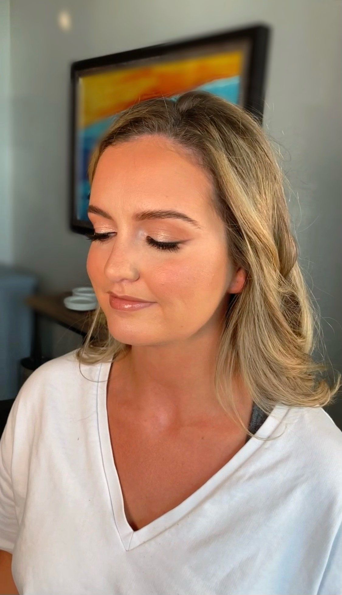 A woman in a white shirt is getting her makeup done in a room.