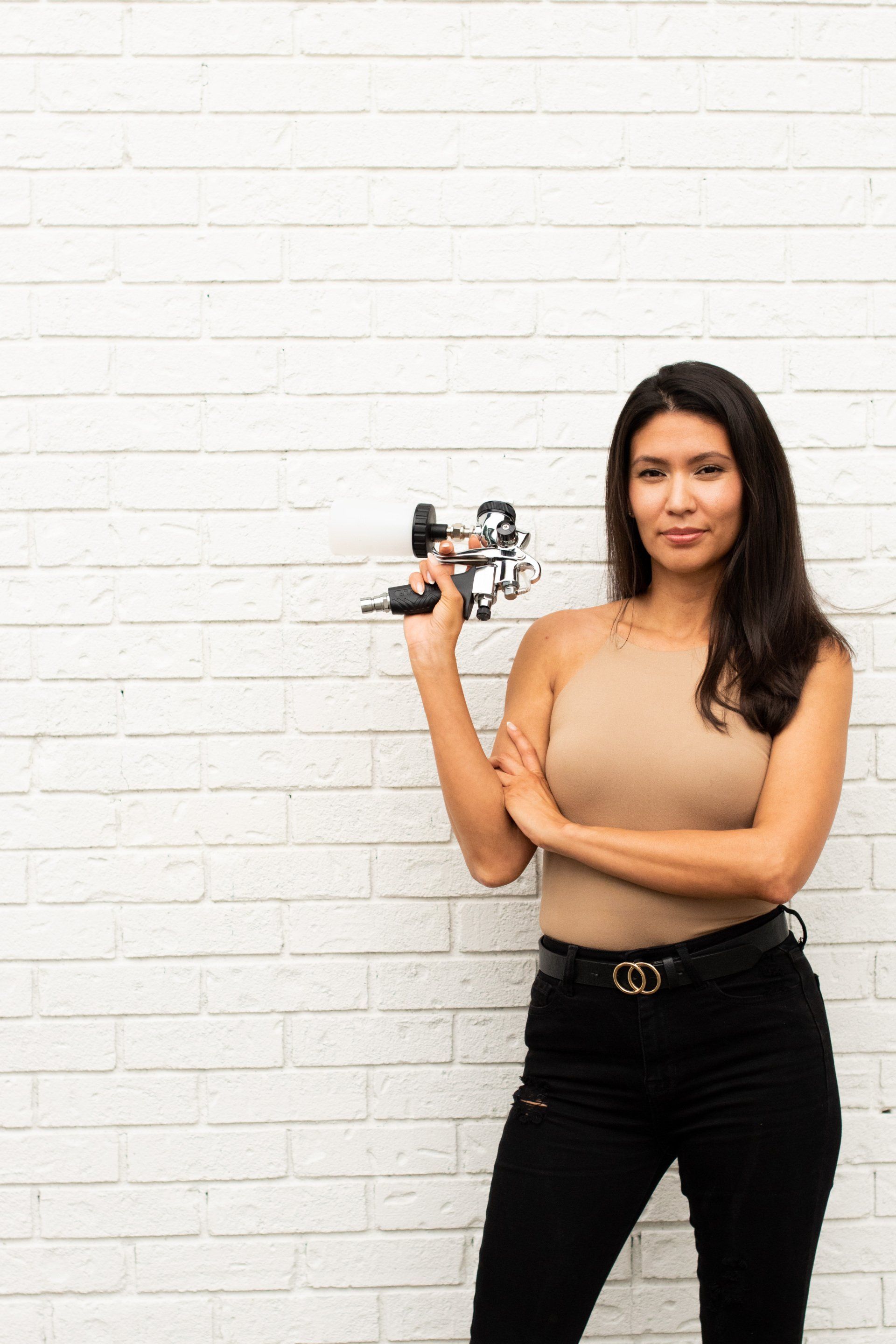 A woman is standing in front of a white brick wall holding a camera.