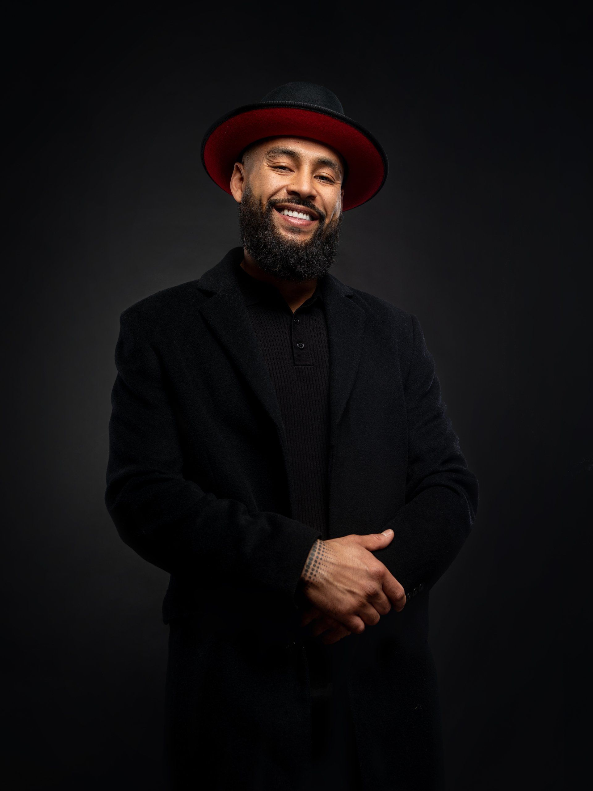 A man with a beard is wearing a black suit and a red hat.