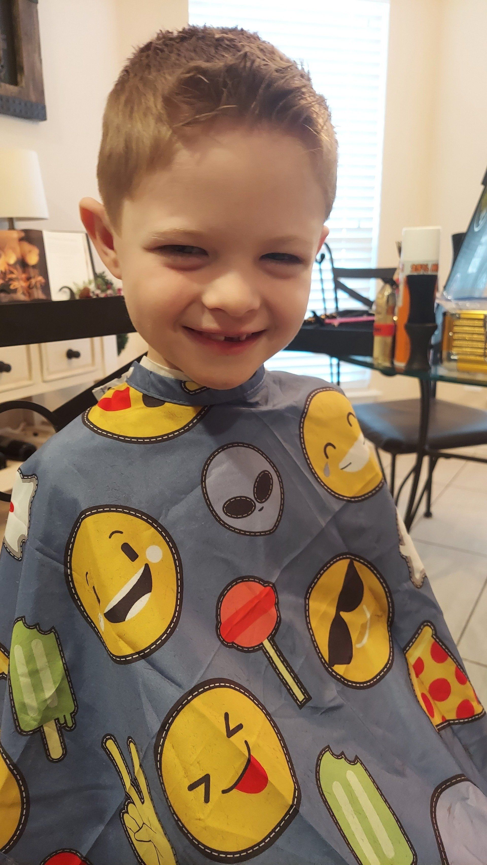 A young boy is wearing a cape with smiley faces on it.