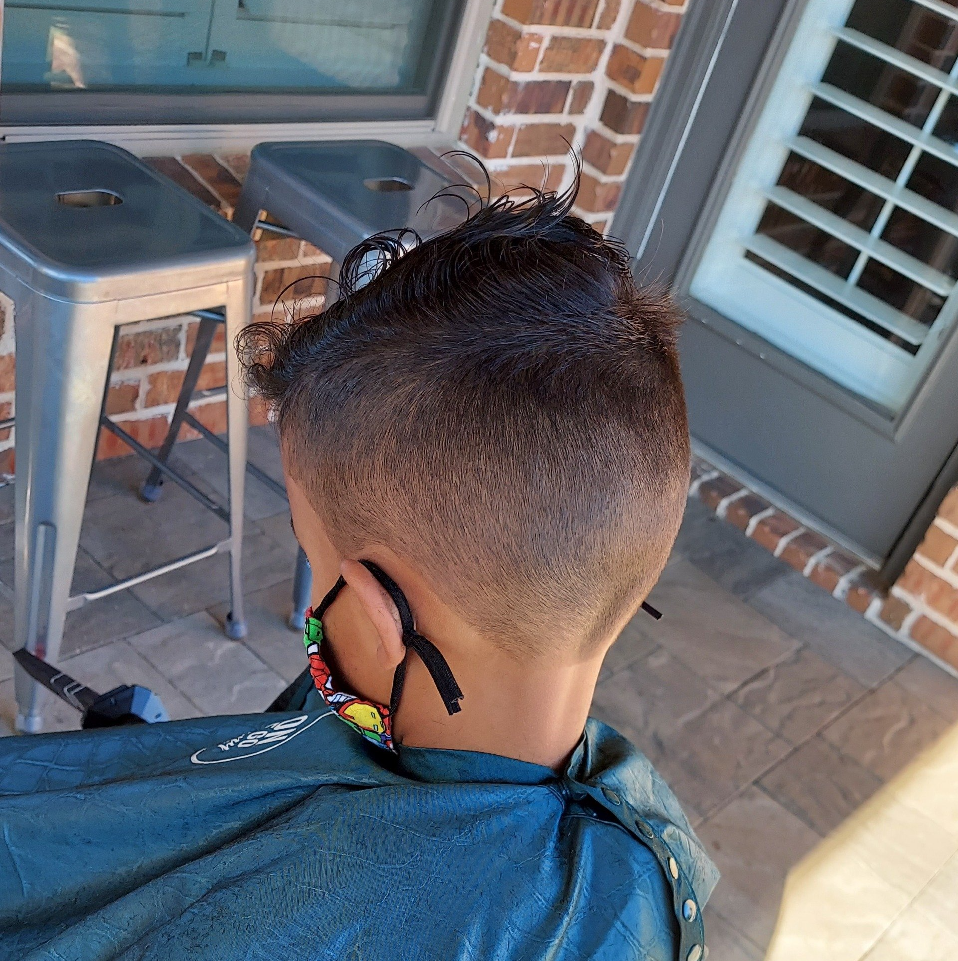 A man wearing a mask is getting his hair cut on a porch.