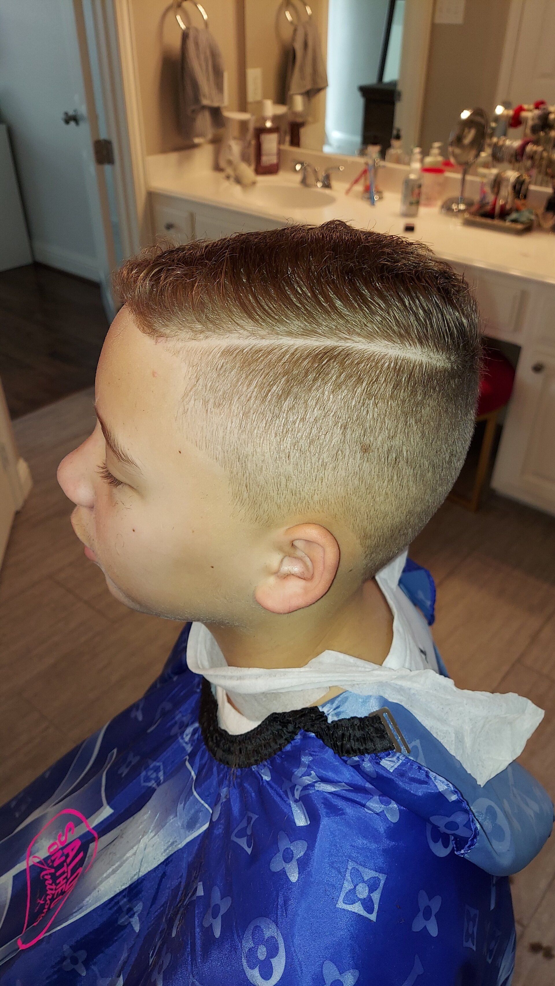 A young boy is getting his hair cut in a bathroom.