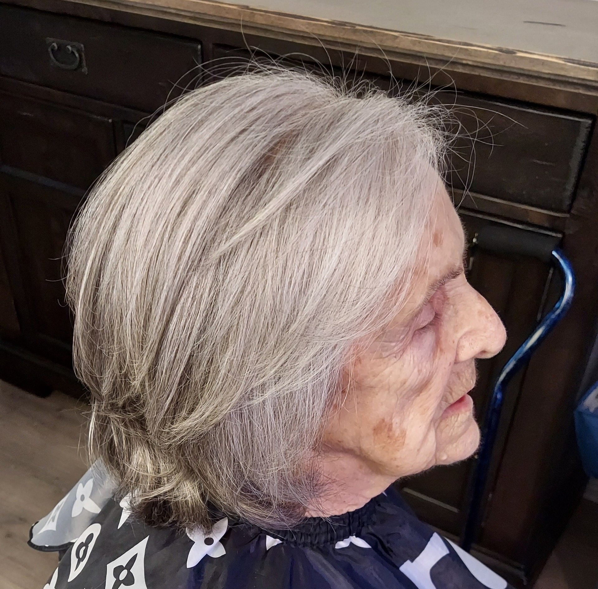 An elderly woman with gray hair is getting her hair cut.