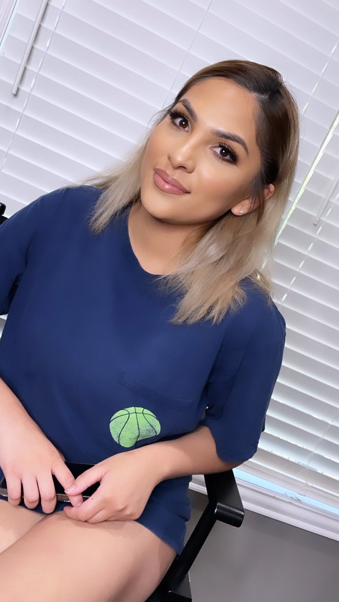 A woman in a blue shirt is sitting in front of a window.