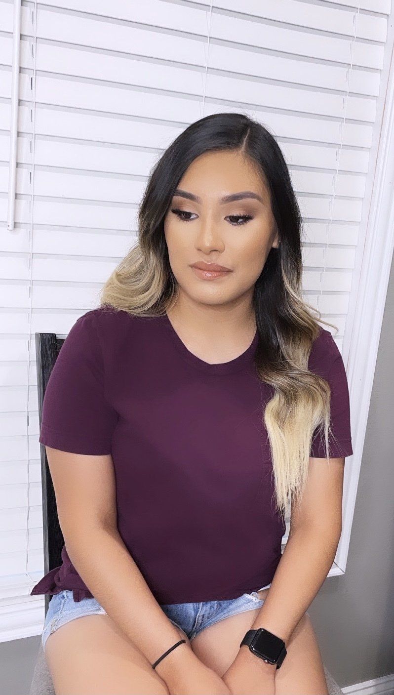 A woman in a purple shirt and shorts is sitting in front of a window.