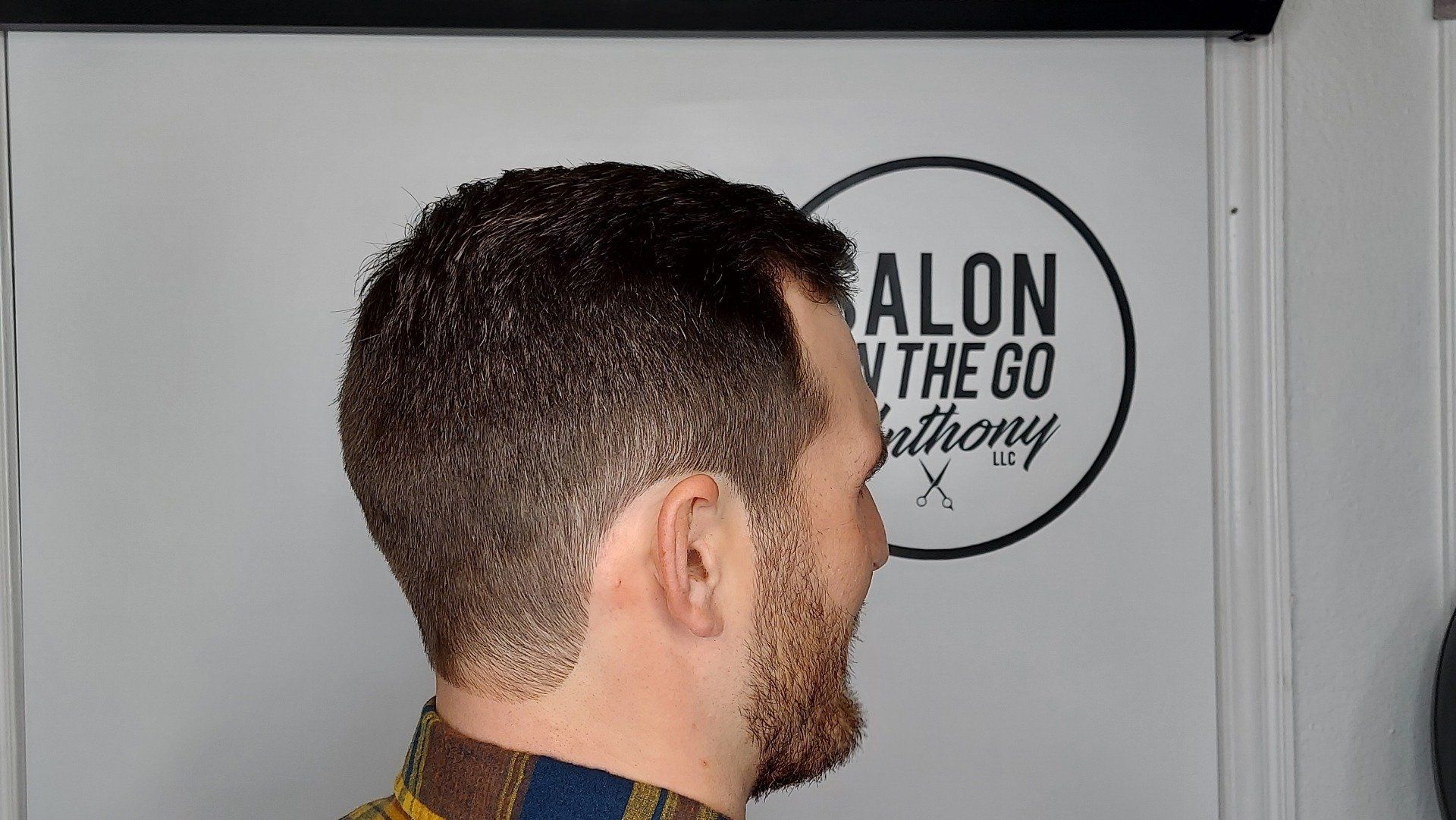A man with a beard is standing in front of a sign that says salon on the go.