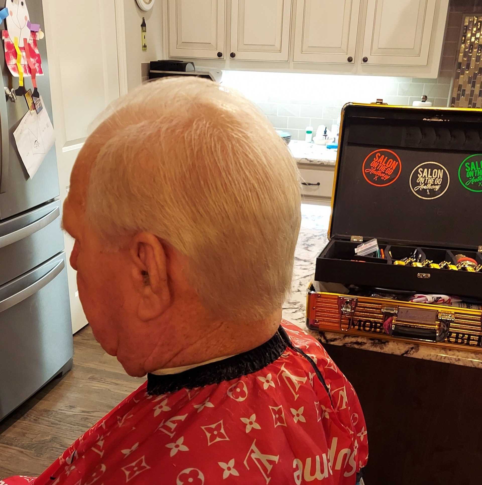 A man in a red louis vuitton cape is getting his hair cut